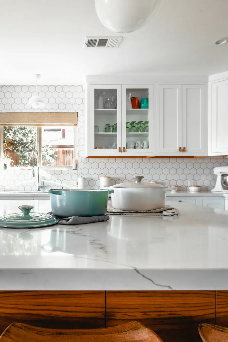 White kitchen with glass-front cabinets, knobs, and a shaded window